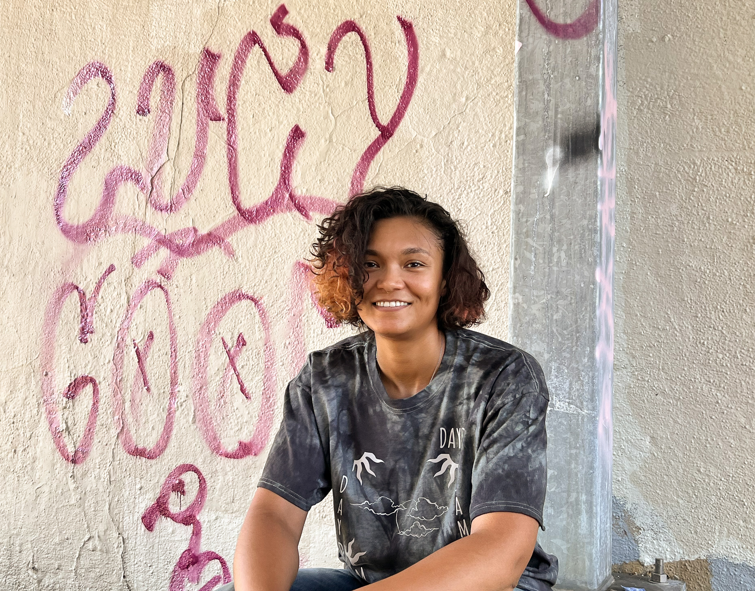 Person smiles while sitting in front of a graffiti wall.