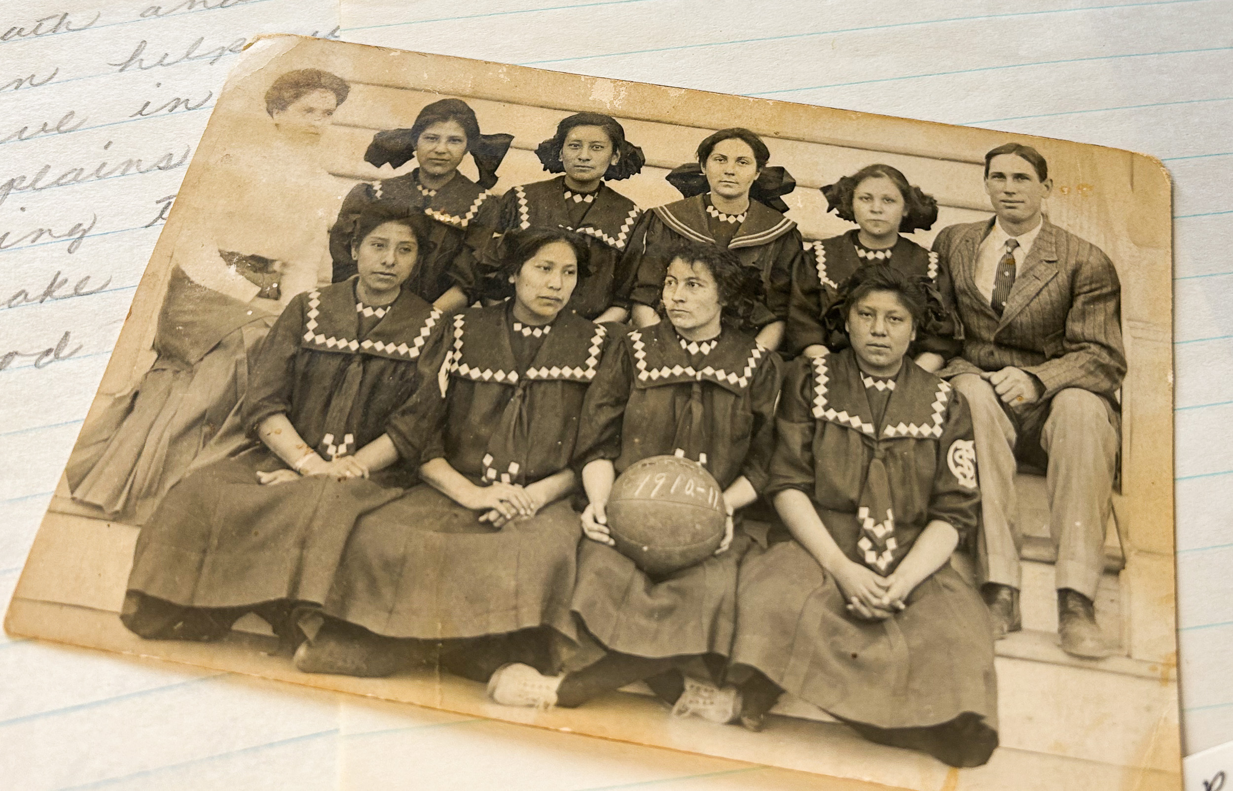 A black and white photo of eight Native American girls sitting together in black dresses.